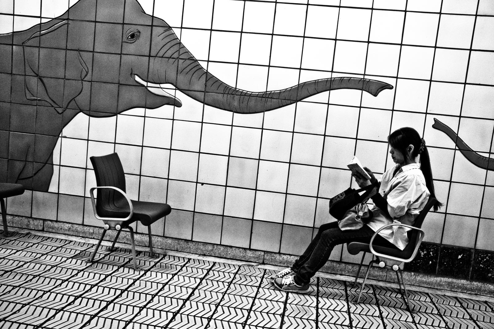 Woman sitting in the metro system of Osaka next to a mural of a elephant. Street Photography by Victor Borst