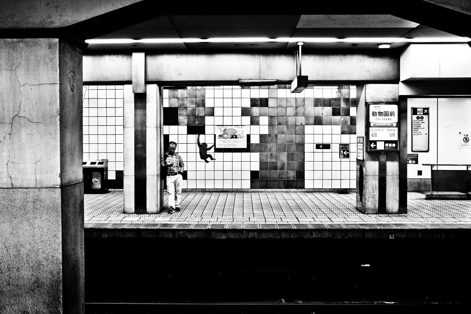 Man standing in the metro system of Osaka next to a mural of a monkey. Street Photography by Victor Borst