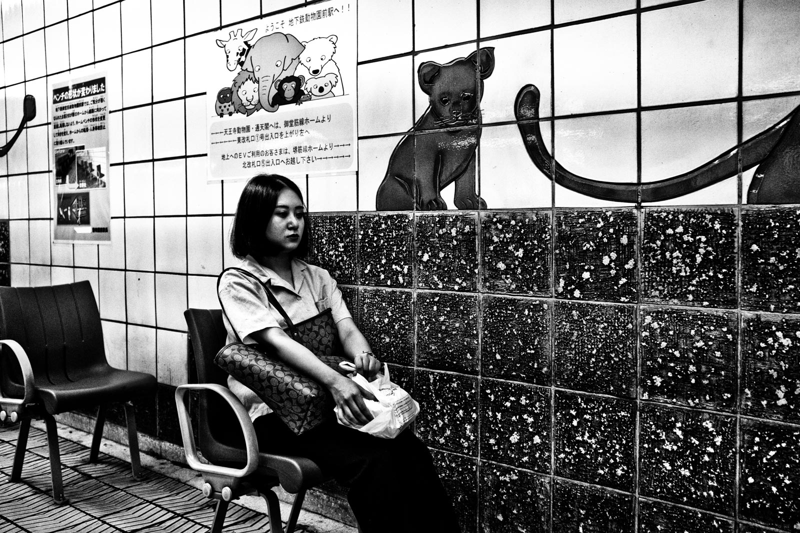 Woman sitting in the metro system of Osaka next to a mural of cub lion. Street Photography by Victor Borst
