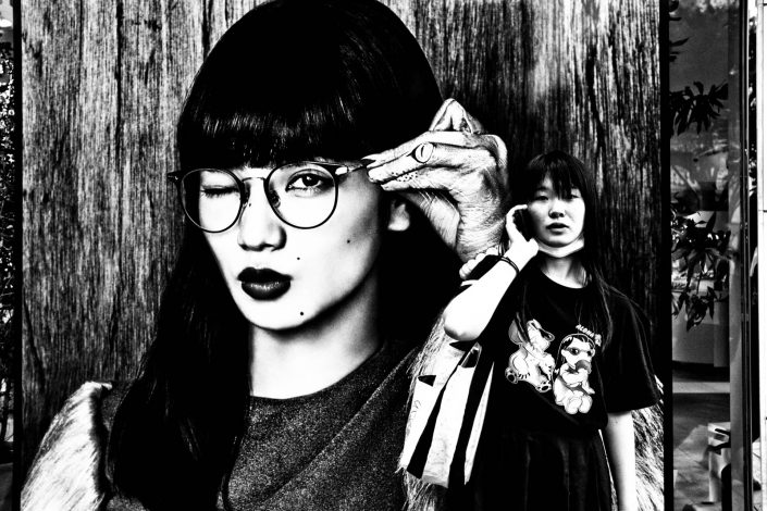 one girl on a billboard with glasses and one real girl with smartphone at Harajuku. Street Photography by Victor Borst