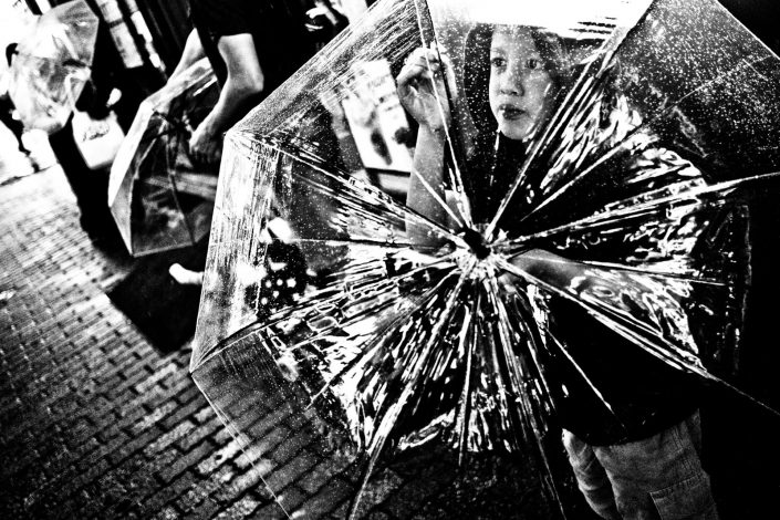 Japanese Girl in rain protecting herself with a see-through umbrella at Shibuya. Street photography by Victor Borst