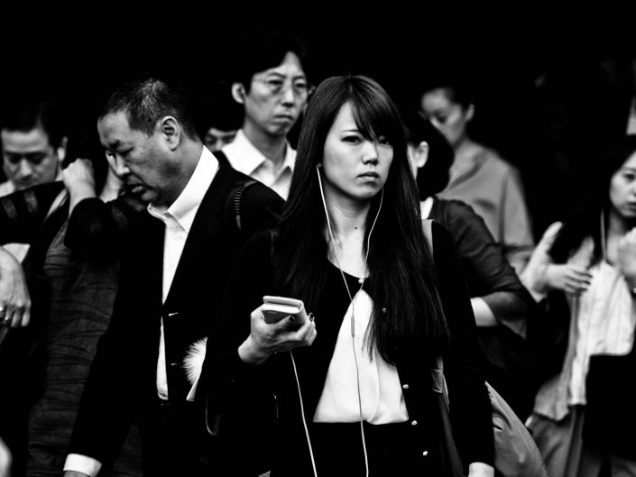 Lots of faces at Shimbashi station with the focus on one woman listening to music. Street Photography by Victor Borst