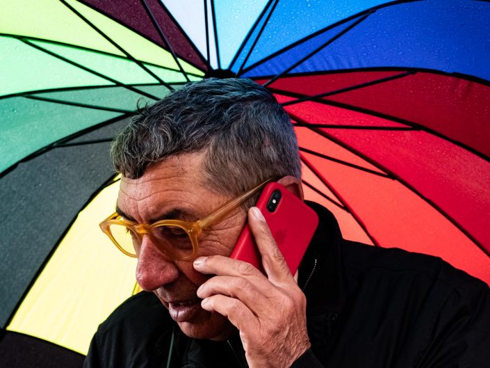 Colorful rainbow umbrella with a man making a phone call. Street photography by Victor Borst